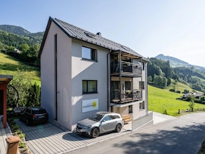 Un immeuble à deux étages doté d’un balcon, avec une voiture garée devant et une enseigne indiquant qu’il s’agit d’un complexe d’appartements.