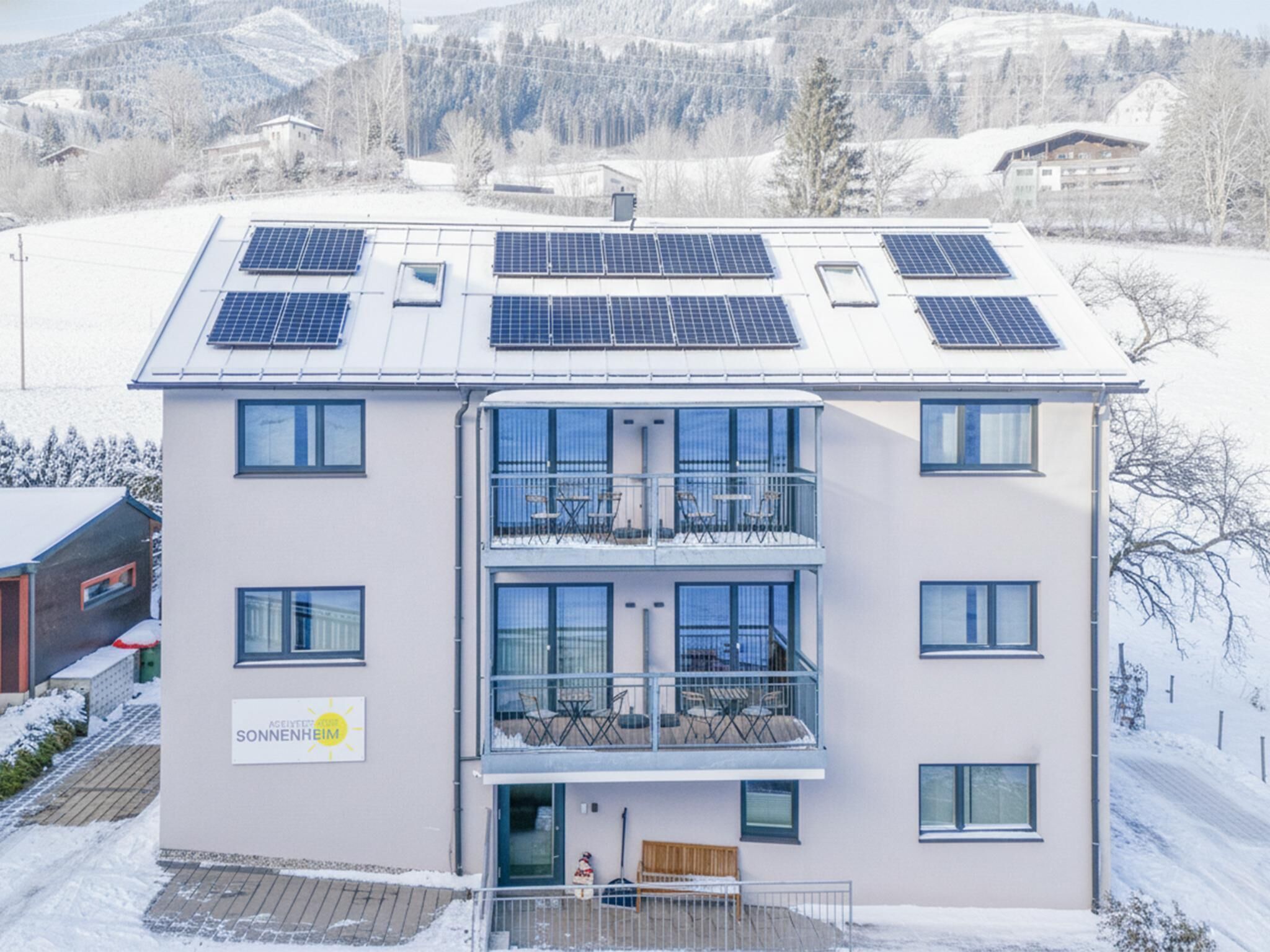 Een modern gebouw met meerdere balkons, zonnepanelen op het dak en een bord waarop zonnecollectie staat.