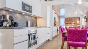 Eine moderne Küche mit integrierten Geräten, ein Essbereich mit rosa Stühlen und ein Holzboden.