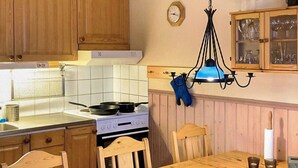A kitchen with wooden cabinets, a stove, a dining table with chairs, a hanging light fixture, and a clock on the wall. - 7 Person Holiday Home in Salen (Transtrand)