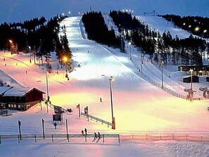 Pista de esqui coberta de neve, com um teleférico, uma cabana de madeira e uma cerca.