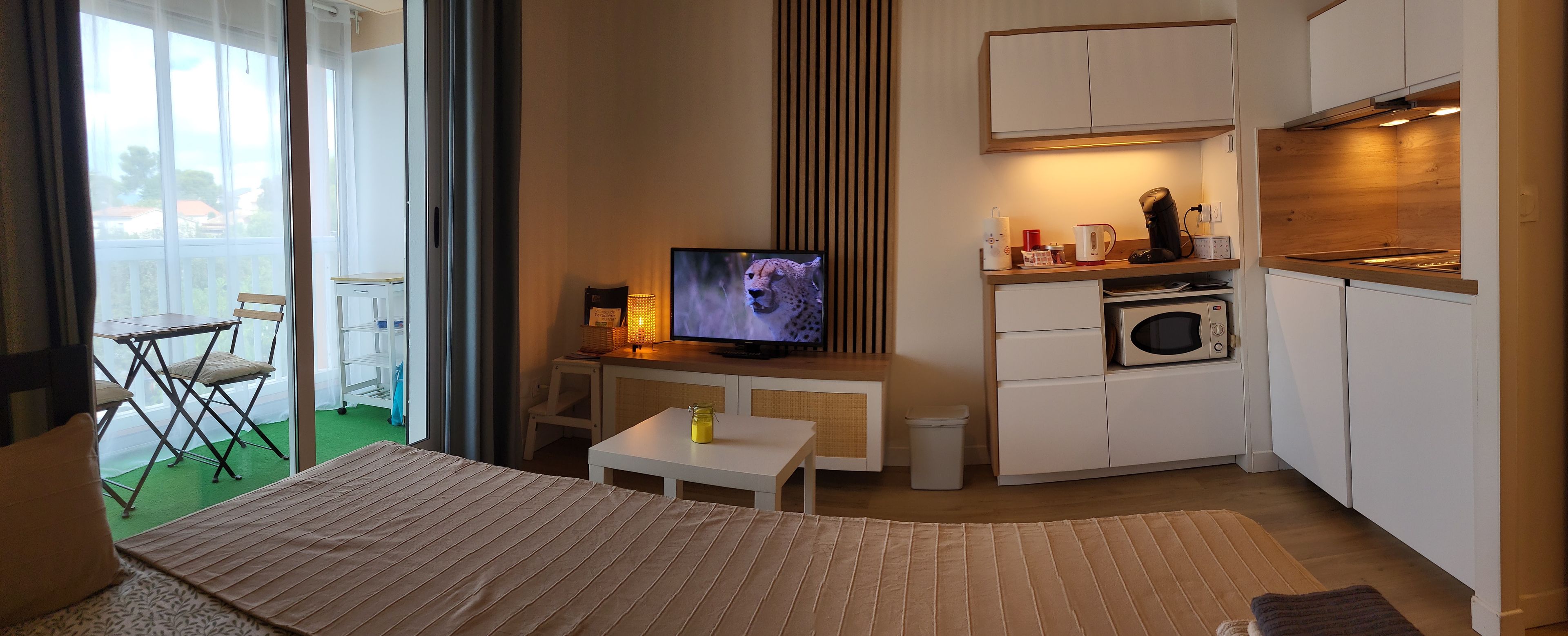 Een compacte hotelkamer met een bed, een televisie, een kitchenette en een klein zitgedeelte.