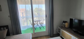 A room with a sliding glass door leading to a balcony, a television on a stand, and a small table with a chair. - A walk to the beach🏖️. Free Wi-Fi🛜. Air-Conditioned Studio in St. Aygulf 🌴 (Fréjus)