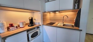 A compact kitchen with a built-in oven, a coffee maker, a kettle, and a sink.