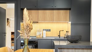 A modern kitchen with wooden cabinets, a central island with a sink, and a vase with dried flowers on the table. - Levandule by Interhome (Abertamy)
