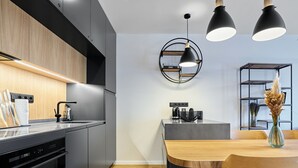 A modern kitchen with dark cabinetry, a wooden countertop, and a built-in oven. There is a dining area with a wooden table and chairs, and pendant lights above. - Levandule by Interhome (Abertamy)