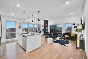 Un apartamento moderno con isla de cocina, comedor y sala de estar, con un amplio ventanal que ofrece vista a la ciudad.