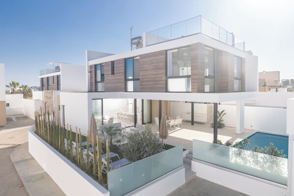 A modern two-story house with a glass balcony, a swimming pool, and a well-maintained garden.