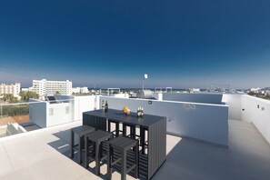 A rooftop terrace with a table and chairs, a flagpole, and a view of the cityscape.