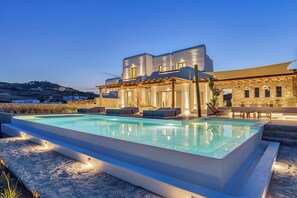 A modern villa with a swimming pool, outdoor seating, and a stone facade.