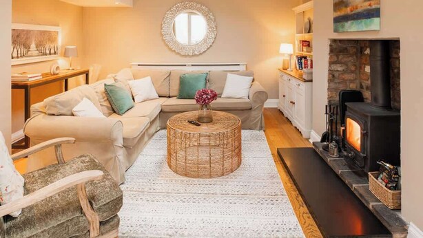 A cozy living room with a sofa, a round coffee table, a fireplace, and a wall-mounted mirror. - Chester coach house with log burner & parking (Cheshire West and Chester)