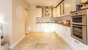 A modern kitchen with white cabinets, a stainless steel oven, and a decorative wall piece. - Chester coach house with log burner & parking (Cheshire West and Chester)