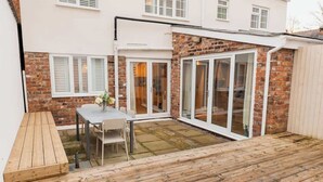 A patio area with a wooden deck, a table with chairs, and a bench. - Chester coach house with log burner & parking (Cheshire West and Chester)
