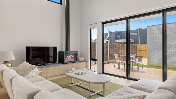 Een moderne woonkamer met een open haard, een bank, een salontafel en uitzicht op de achtertuin door grote schuifdeuren.