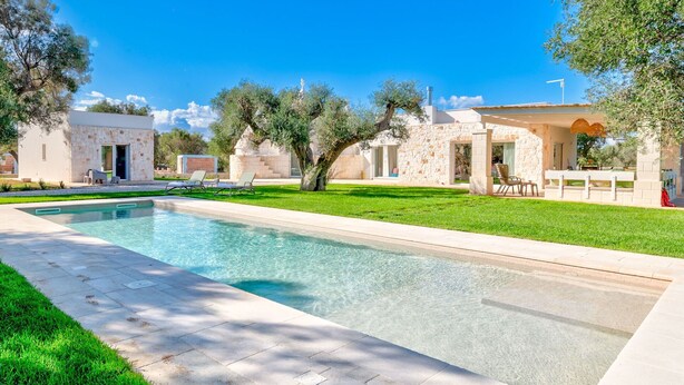 A swimming pool with lounge chairs, a stone building, and a well-maintained lawn.