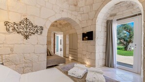 A room with stone walls, a bed, a TV, and a view of the outdoors.