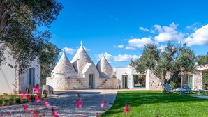 A stone building with conical roofs, a paved driveway, and a grassy area with pink flowers.