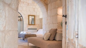 A bedroom with a stone wall, a bed, a sofa, and a mirror.