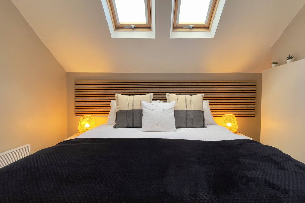 A bedroom with a bed, two skylights, a headboard with horizontal slats, and bedside lamps.