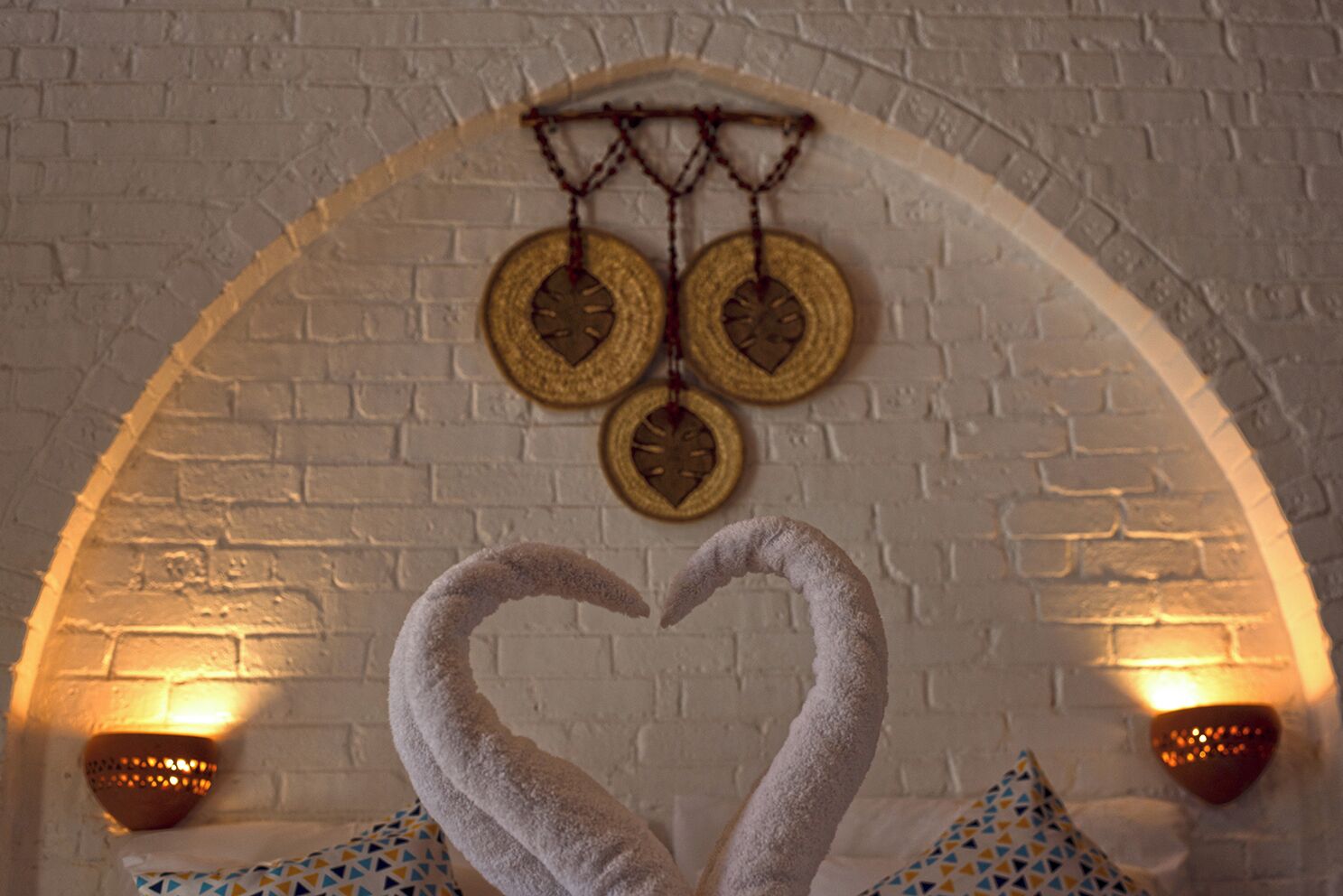 Une pièce avec un mur en briques blanches, une décoration en forme de cœur réalisée avec des serviettes et deux lampes fixées au mur.