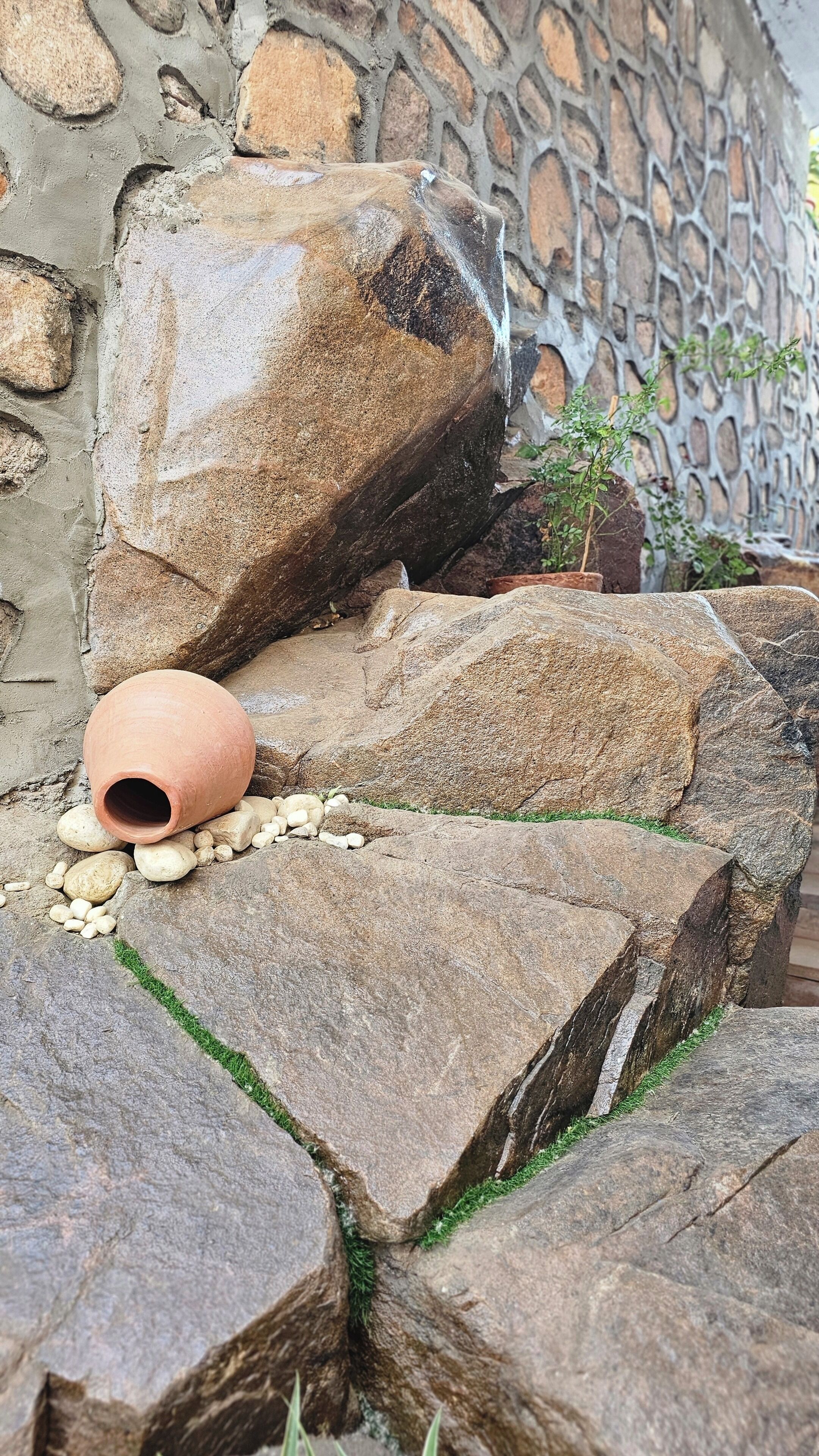 A rustic outdoor setting with large rocks, a clay pot, and a small potted plant.