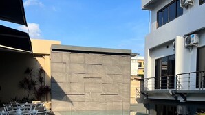 Ein Außenpoolbereich mit weißen Liegestühlen und Tischen, einer Steinmauer und einem Gebäude mit Klimaanlagen.