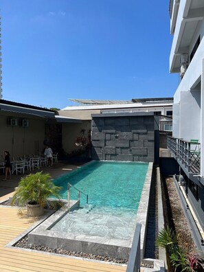 A swimming pool with a stone wall, surrounded by a deck area with chairs and potted plants. - Karon Boutique (Karon)