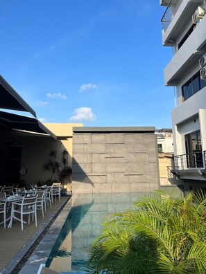 An outdoor pool area with a stone wall, white chairs, and tables arranged for dining. - Karon Boutique (Karon)