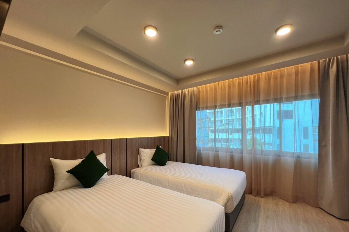 A hotel room with two beds, a large window with curtains, and recessed ceiling lighting.
