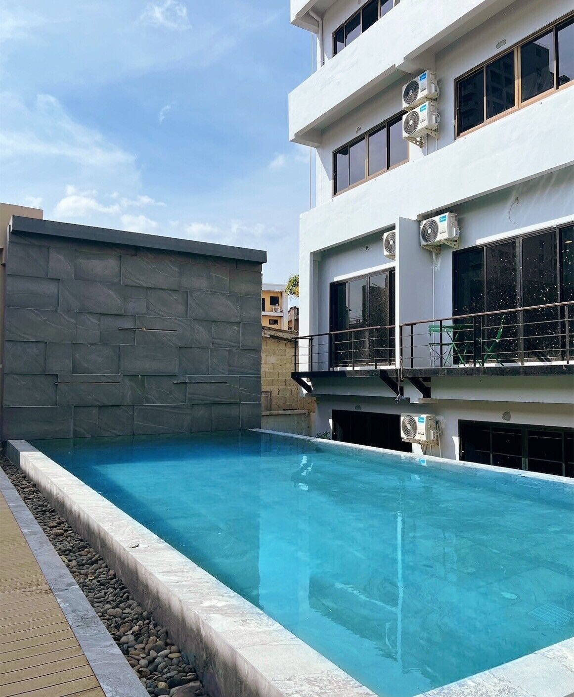 A modern building with a rooftop pool, air conditioning units, and a stone wall.