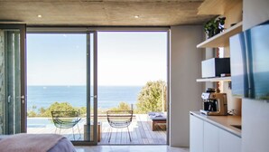 Un dormitorio moderno con un amplio ventanal corredero que da a una terraza exterior con vistas al mar.