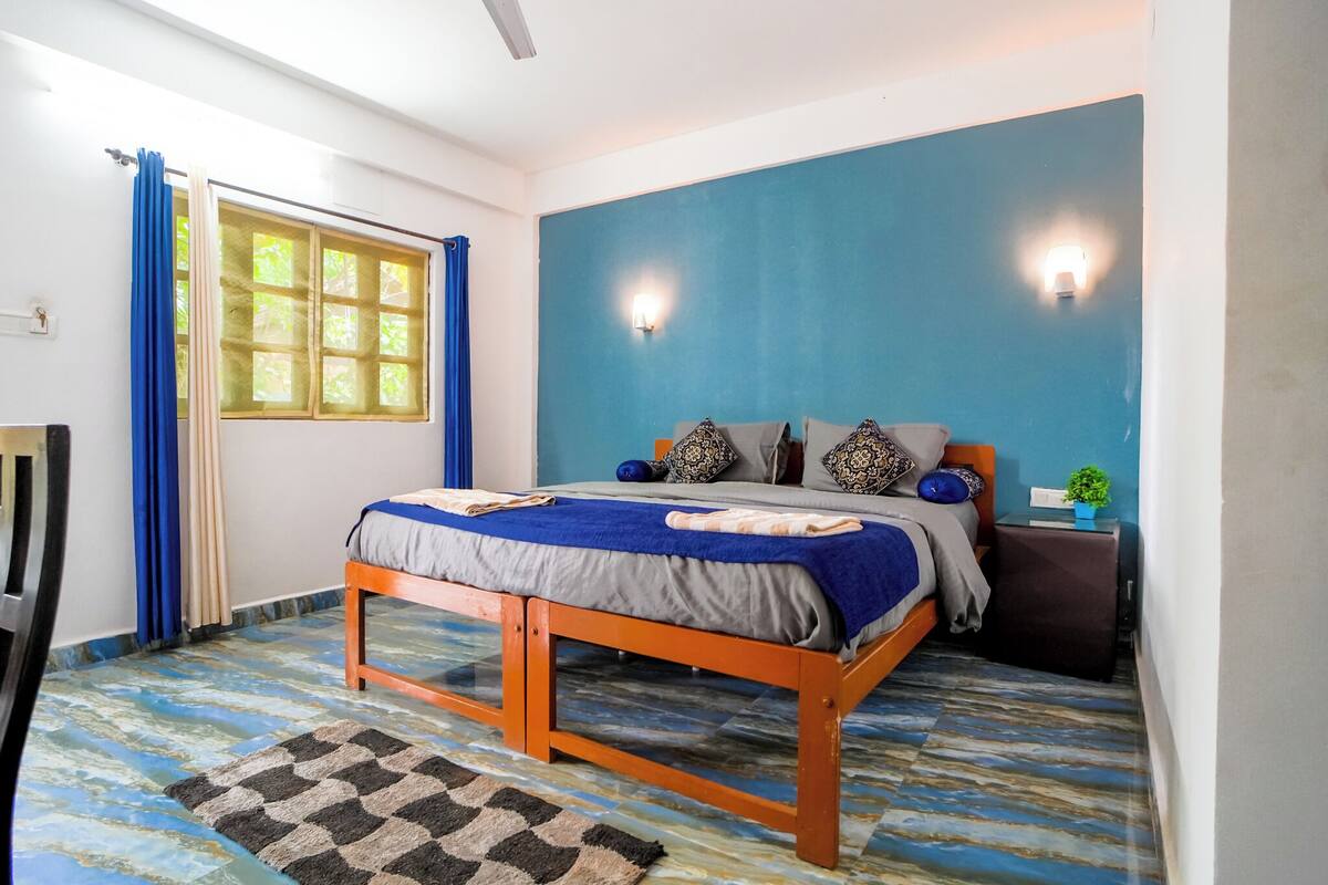 Een slaapkamer met een bed, gordijnen, een nachtkastje en een wandlamp.