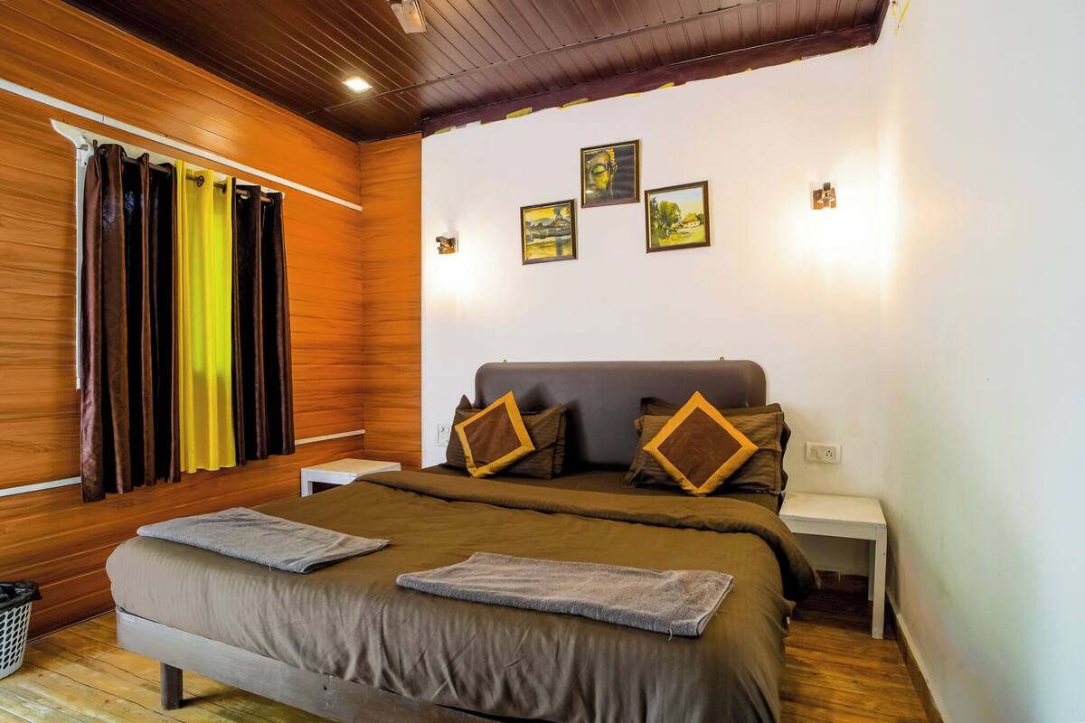 Een slaapkamer met een houten plafond, een bed met bruin beddengoed, twee nachtkastjes en drie ingekaderde foto's aan de muur.