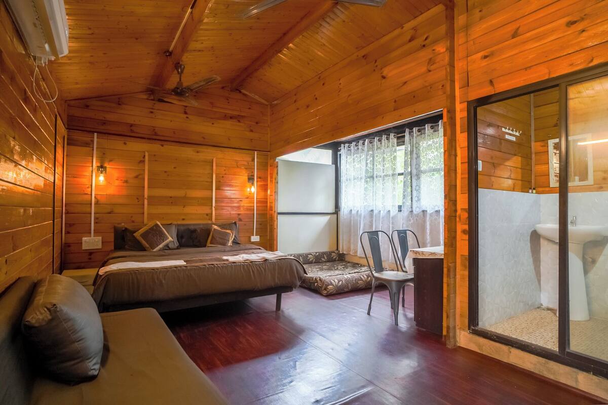 Een houten kamer met twee bedden, een bank, een stoel en een badkamer met wastafel en toilet.