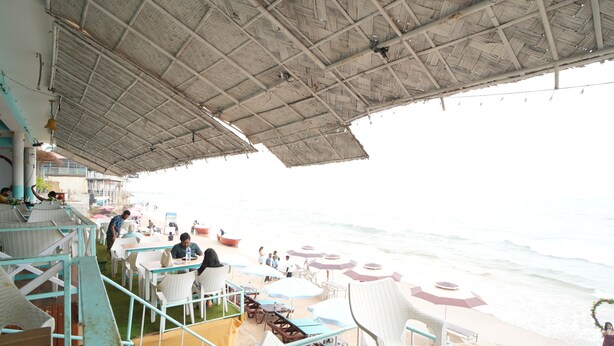 En restaurang vid stranden med uteservering, ett halmtak och utsikt över havet.