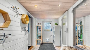 A narrow hallway with white wooden walls, a grey carpet, and a fur rug. There are shelves with plants and a mirror on the right.