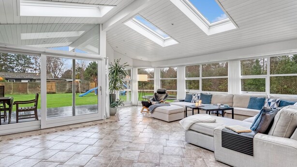A spacious sunroom with large windows, a comfortable seating area, and a view of a backyard with a slide.