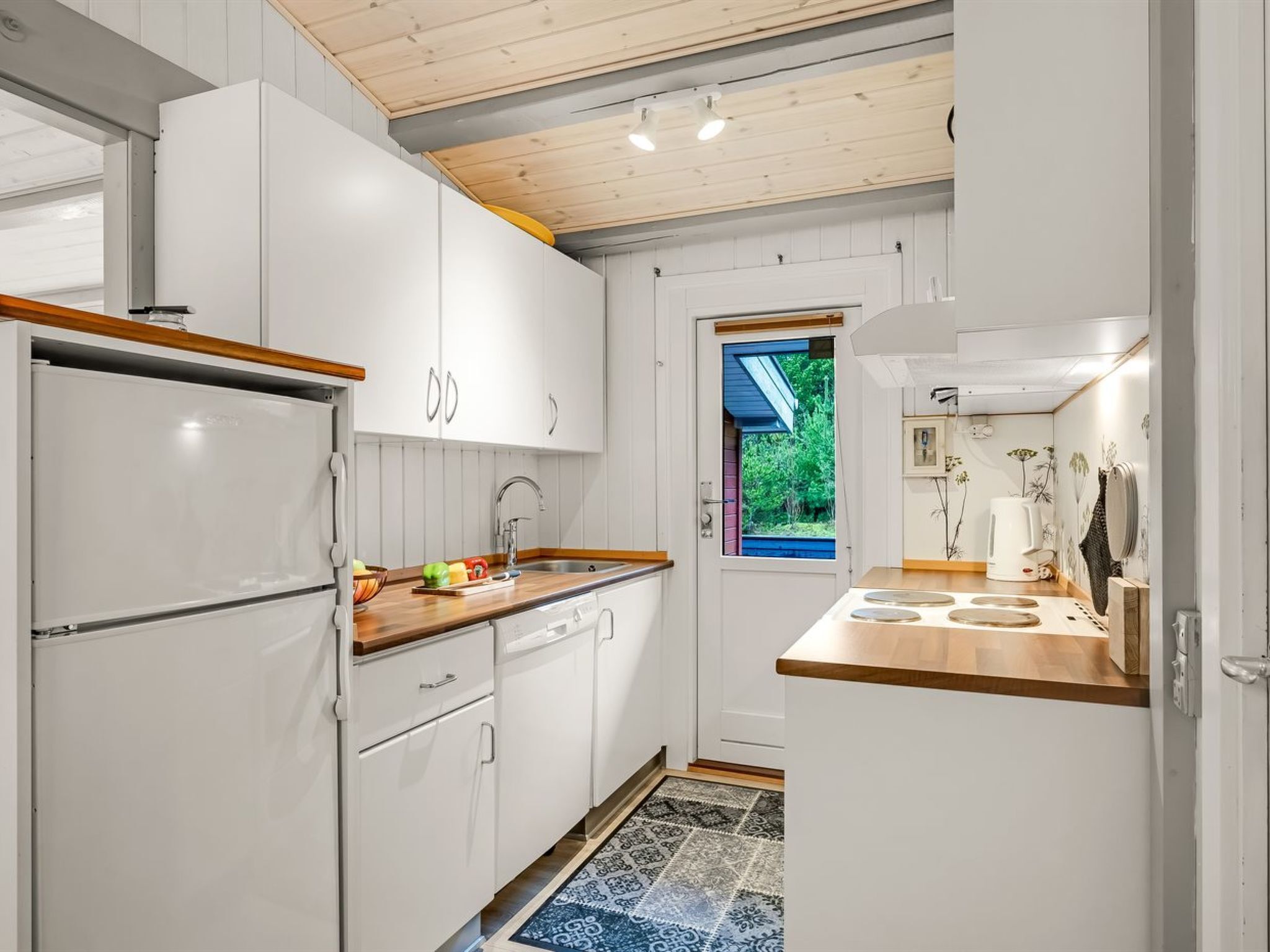 Une cuisine moderne avec des armoires blanches, un plan de travail en bois, un four encastré et une fenêtre donnant sur un paysage verdoyant.