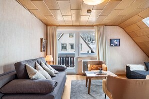 A cozy room with a sofa, a chair, a table, and a window with a view of buildings.