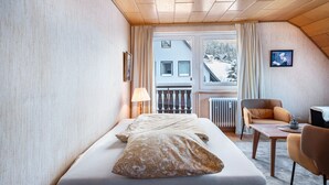 A bedroom with a bed, a chair, a table, a window with a view of a building, and a radiator. - Apartment '4, 65 Qm' with Shared Garden, Balcony and Wi-Fi (Lenzkirch)