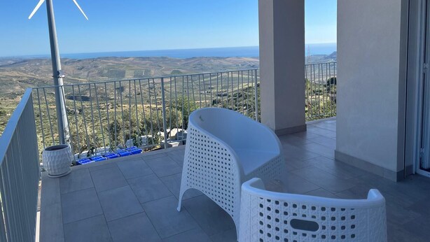 A balcony with a wind turbine, white wicker furniture, and a view of the countryside. - TENUTE LAZZARINO (Sciacca)