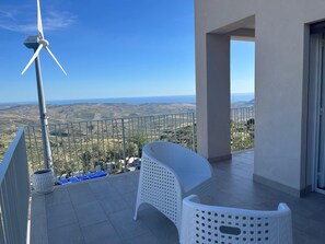 A balcony with a wind turbine, white wicker furniture, and a view of the countryside. - TENUTE LAZZARINO (Sciacca)