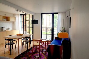 A modern kitchen with a dining area, a large window with curtains, and a television on the wall.