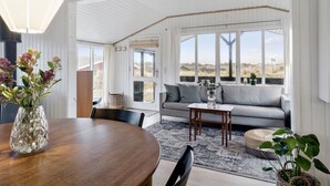 A spacious living room with a large window, a wooden dining table, and a grey sofa.
