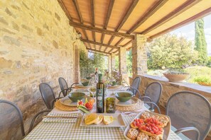 An outdoor dining area with stone walls, wooden beams, and a view of greenery.
