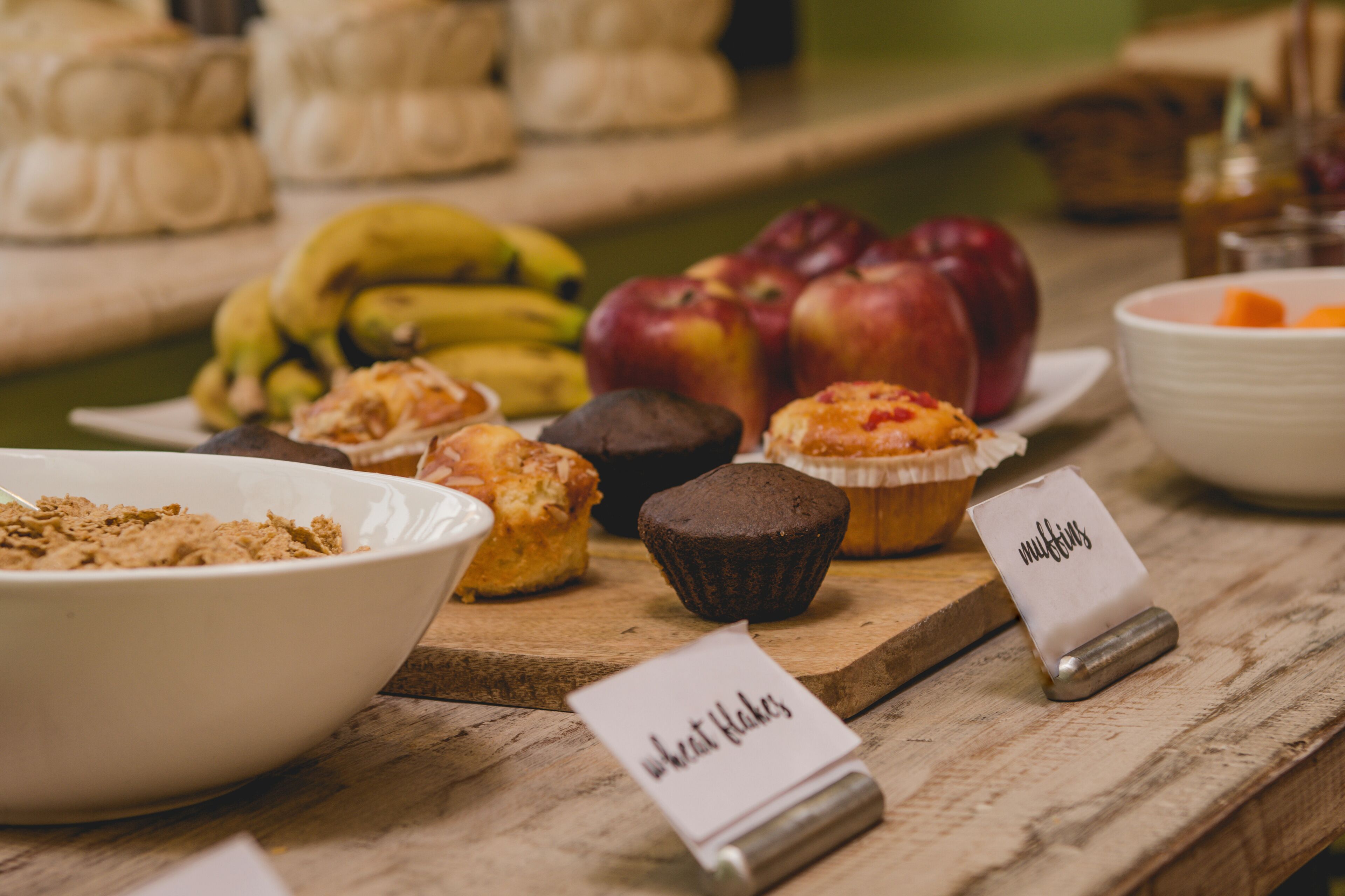 Une table en bois sur laquelle sont disposés divers produits de boulangerie, notamment des muffins et un bol de céréales.