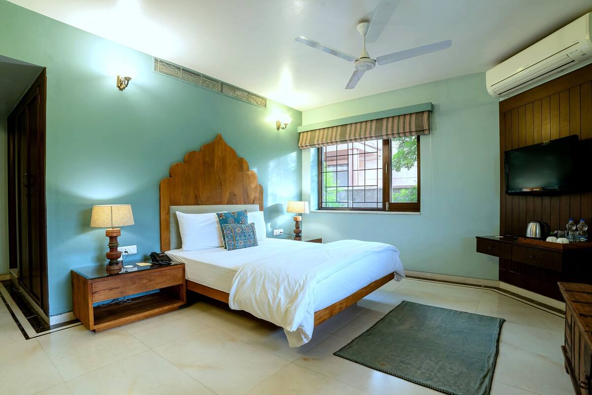 A bedroom with a bed, bedside tables, a nightstand, a ceiling fan, an air conditioning unit, a TV, and a window with a view.