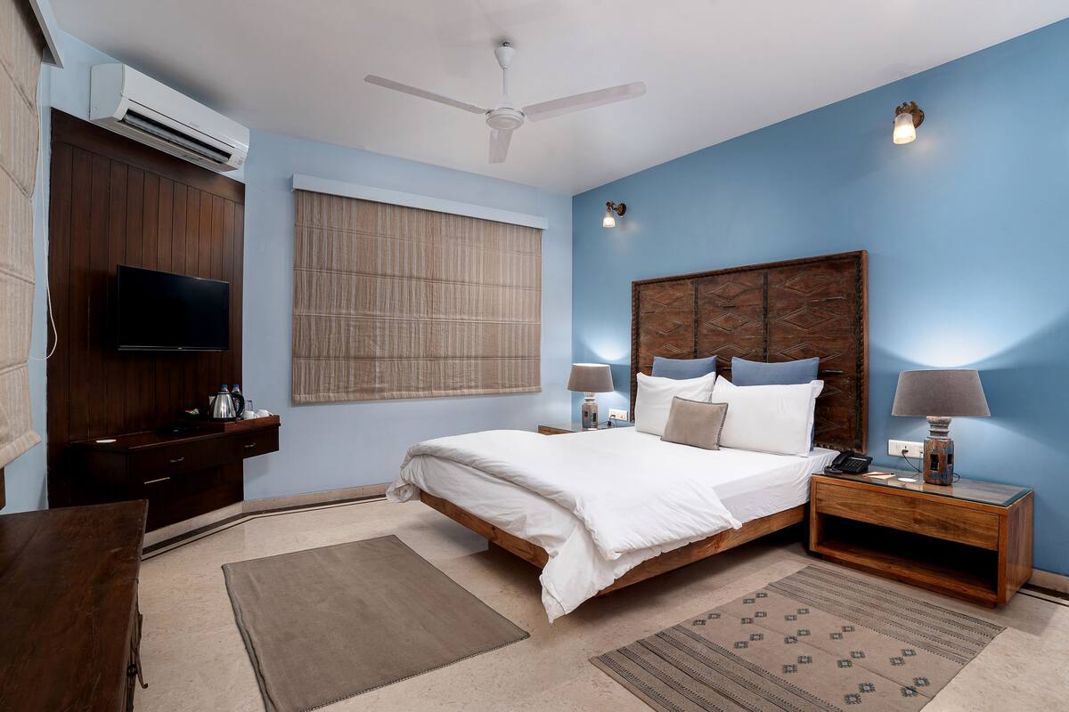 A bedroom with a bed, bedside tables, a TV, and an air conditioning unit.