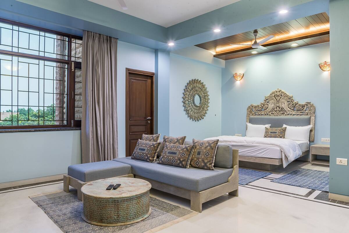 A bedroom with a bed, a sofa, a round coffee table, and a decorative mirror on the wall.