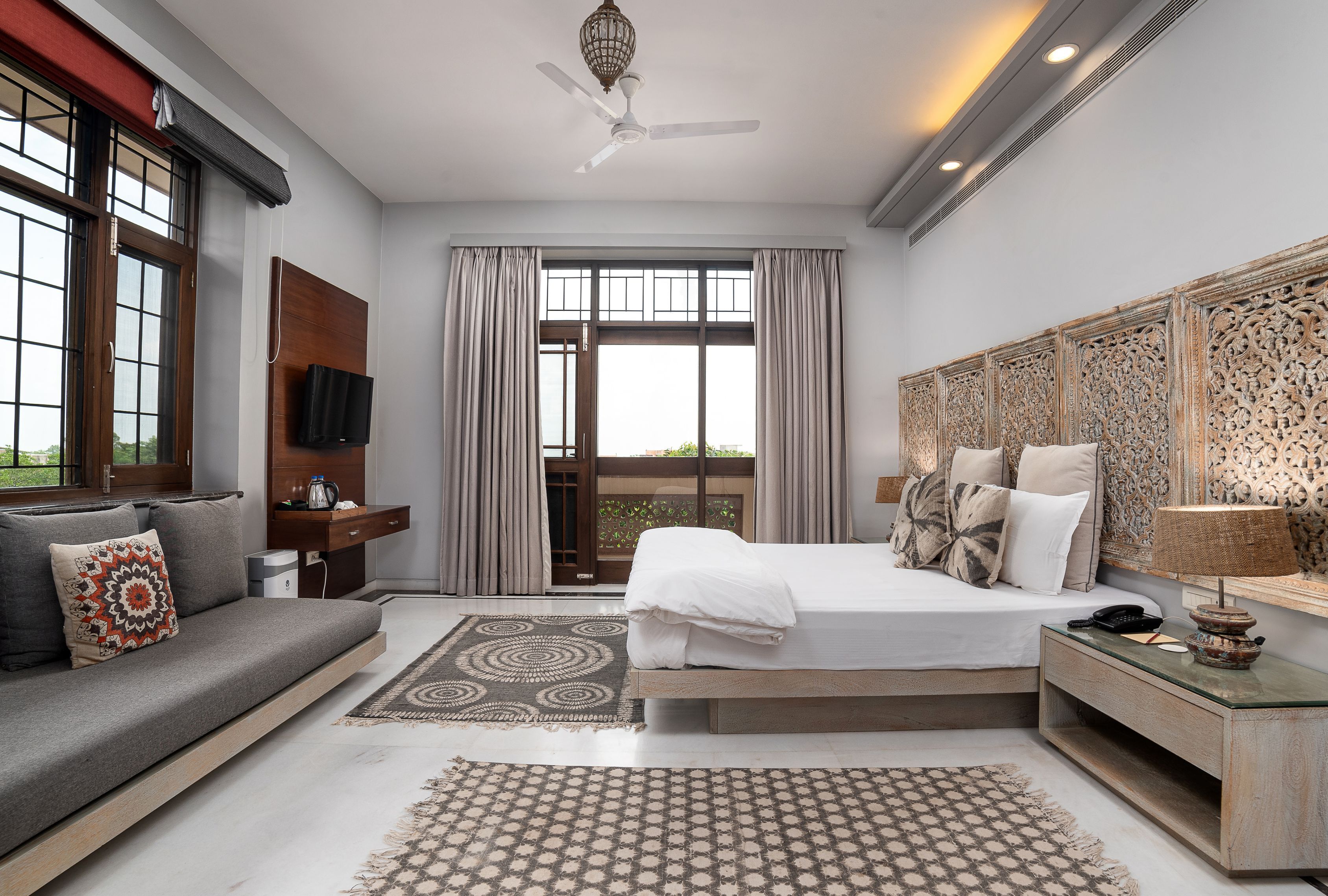 A modern hotel room with a bed, sofa, TV, and a balcony view.